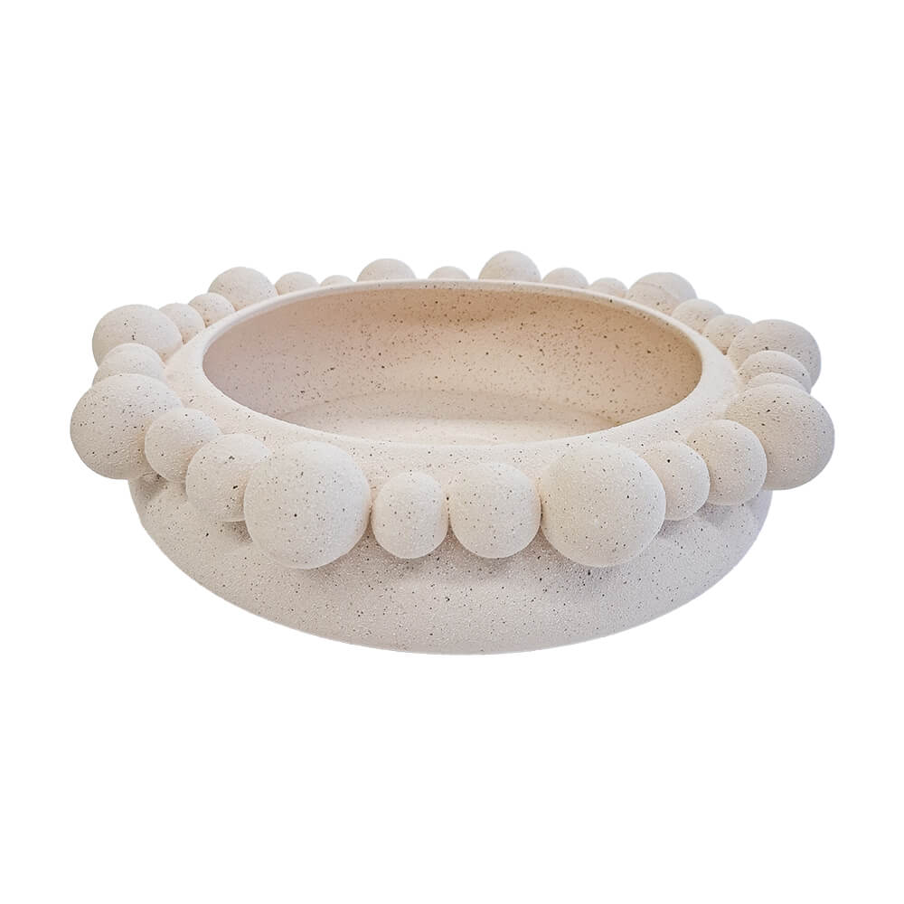 Centro de mesa redondo de cerâmica na cor marfim (natural), apresentando uma textura externa rica composta por diversas esferas em relevo. A peça possui tamanho de 35 cm de largura e 10 cm de altura, com design atemporal e acabamento rústico que destaca as variações únicas de cada peça. Como deve ser usado: ideal para compor a decoração de mesas de jantar ou centros de sala, sendo perfeito para acomodar frutas, esferas decorativas ou ser usado como uma peça de destaque chic e com personalidade.